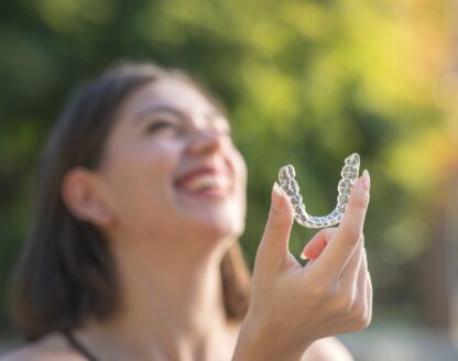 Beautiful smiling Turkish woman is holding an invisalign aligner in alpha nj 