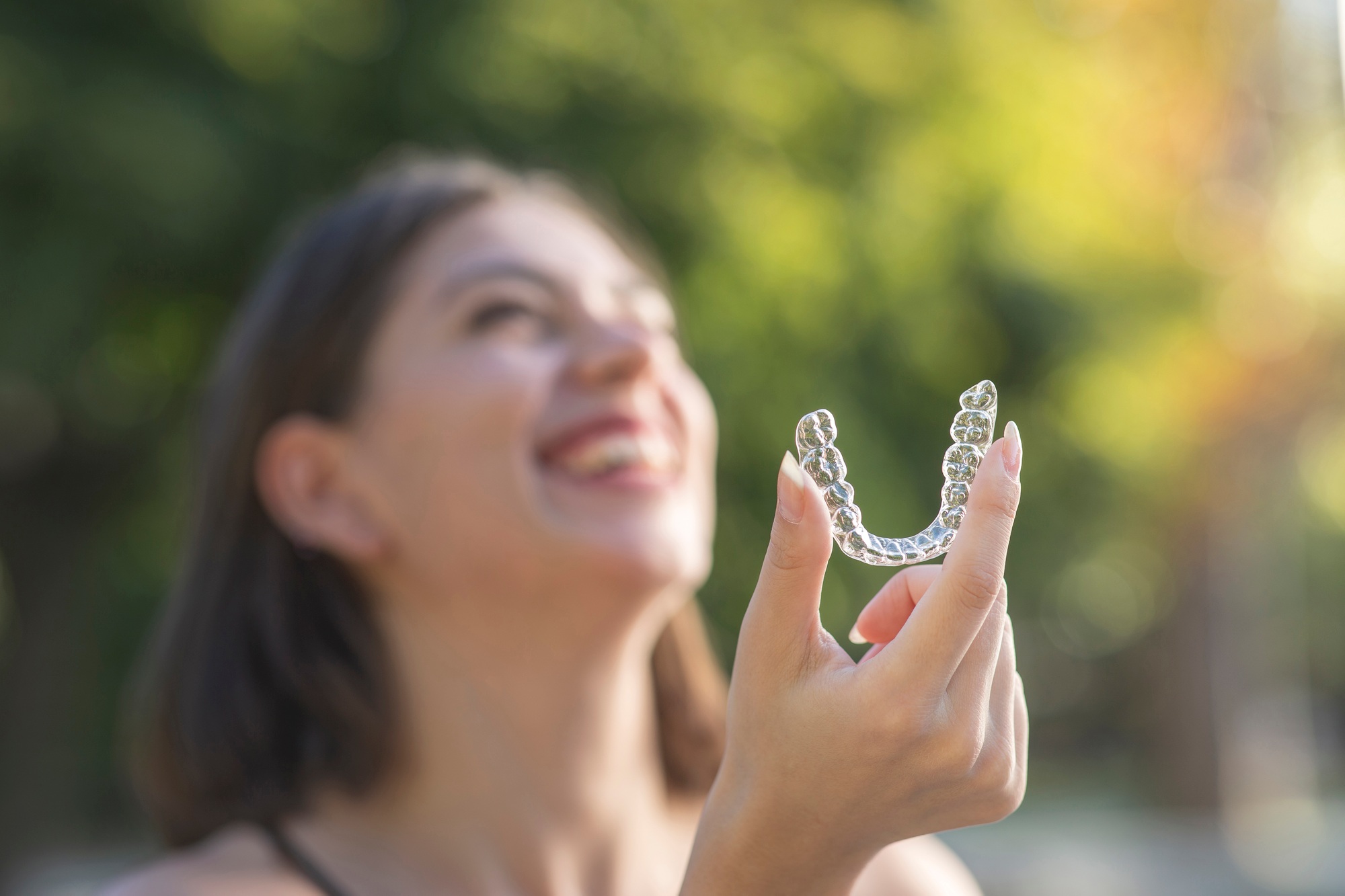 Beautiful smiling Turkish woman is holding an invisalign aligner in alpha nj